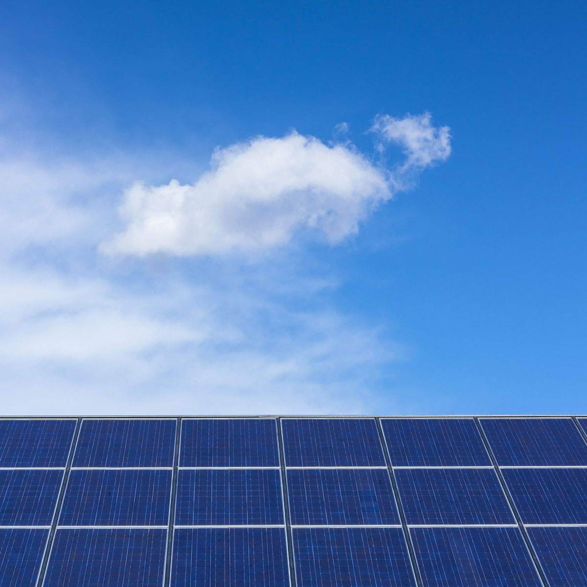 Dach mit Solarpanels im unteren Drittel des Bildes. Blauer Himmel mit kleinen weißen Wolke.